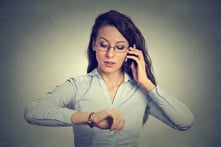 Business and time management concept. Young businesswoman looking at wrist watch, talking on mobile phone running late for meeting. Time is money